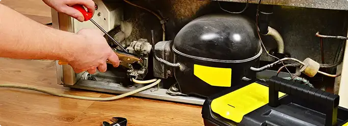 Refrigerator repair technician fixing the compressor and wiring in Lexington, SC