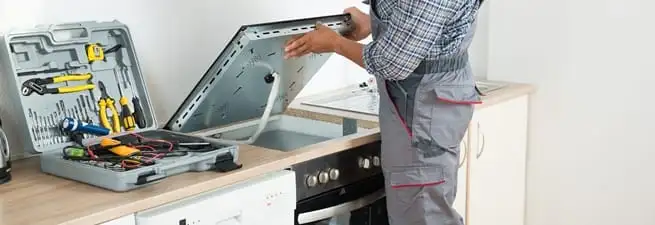 Cooktop repair technician lifting a built-in stovetop for service in Columbia, SC