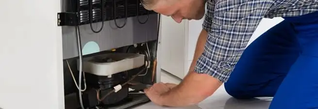 Refrigerator repair technician servicing the compressor and condenser area in Columbia, SC