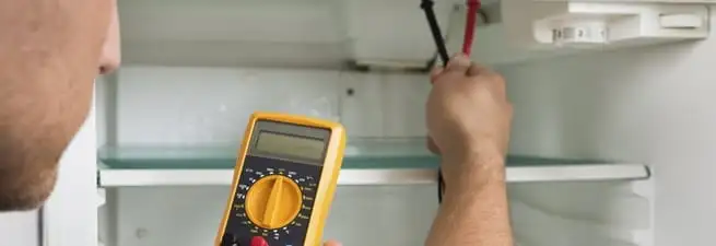 Refrigerator repair technician testing electrical components with a multimeter in Columbia, SC